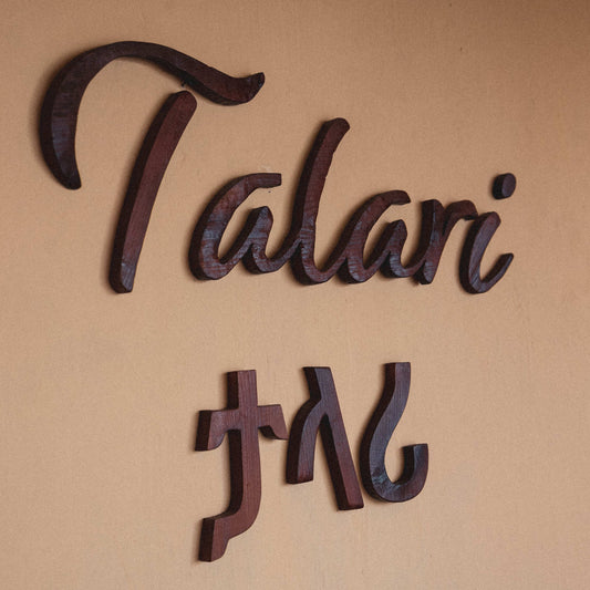Image of a logo made of wood on a wall in the Talari addis store. The logo reads "Talari" written in English and Amharic